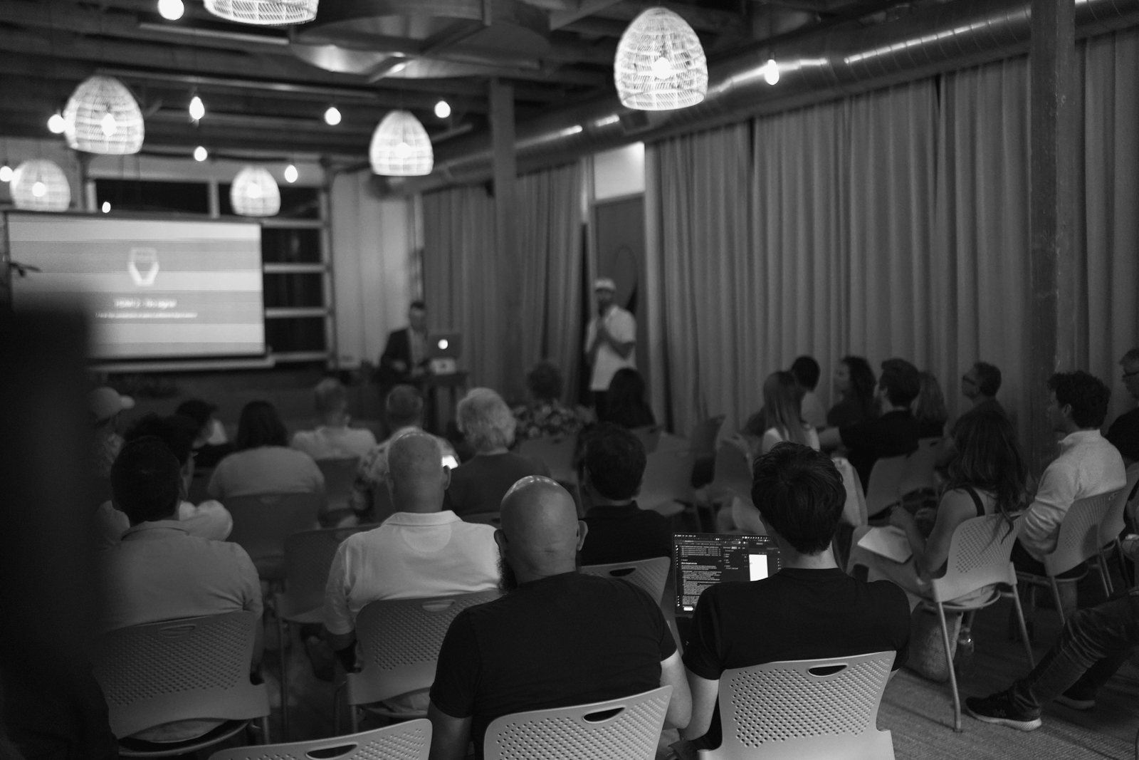 The room at Claude Code for Founders in Santa Barbara, photographed from the back: rows of seated attendees facing a lit screen, one laptop open mid-row.